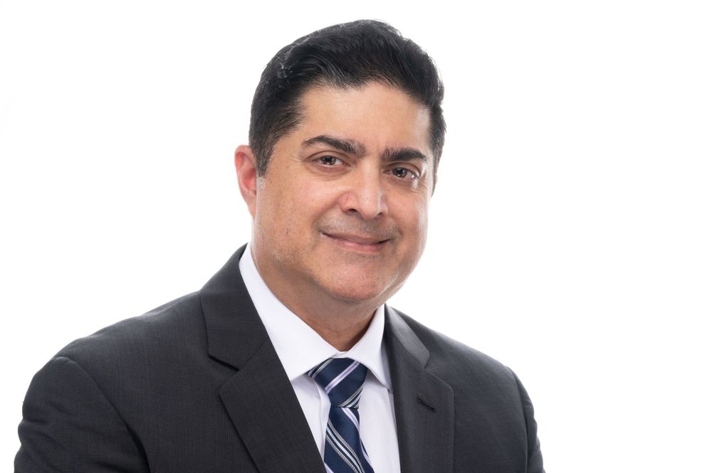 Professional portrait of person in dark suit and blue tie against white background.