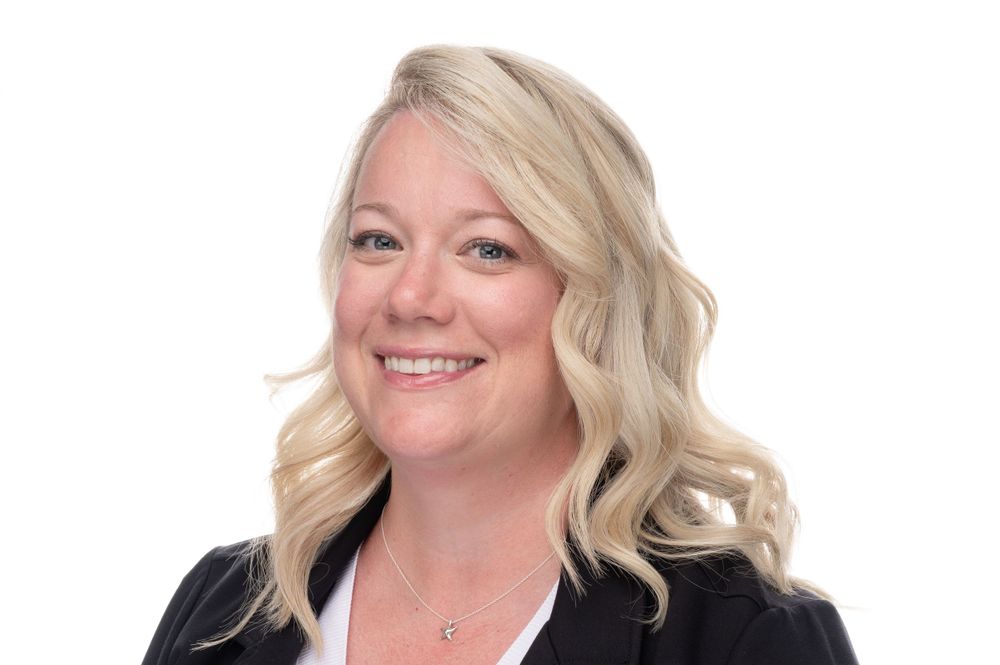 Professional headshot of person with blonde wavy hair wearing black blazer.
