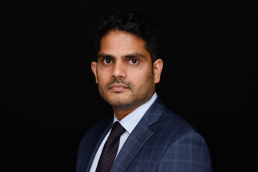 Professional business portrait of person in navy suit against dark background.
