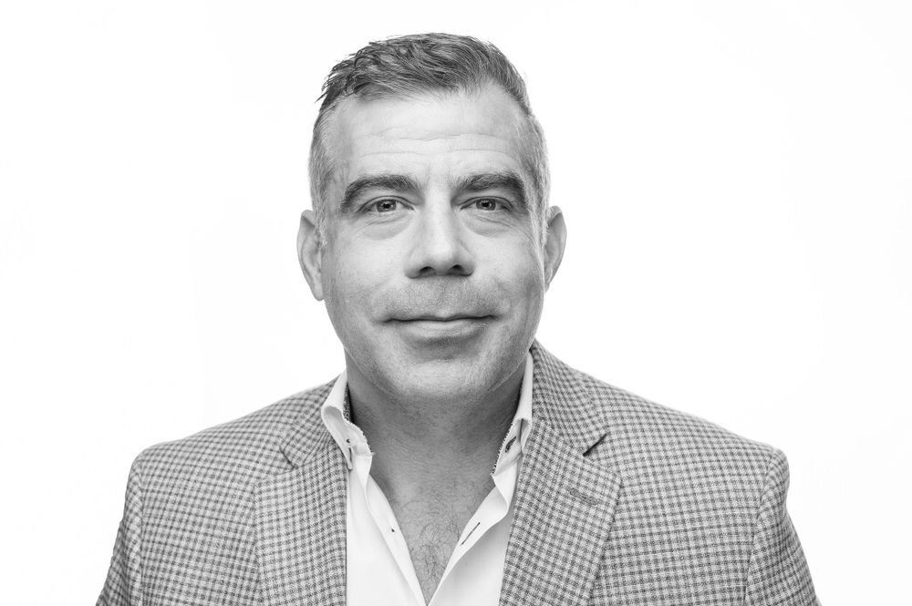Professional headshot of someone in a checkered blazer against a white background.