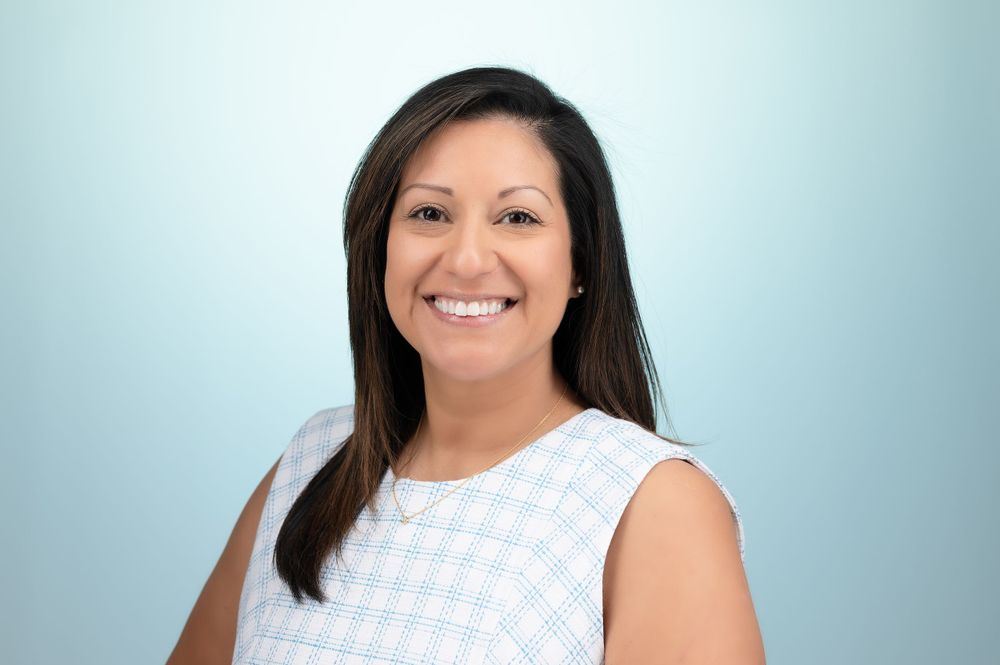 Professional headshot of a person in a white sleeveless top against a light blue backdrop.