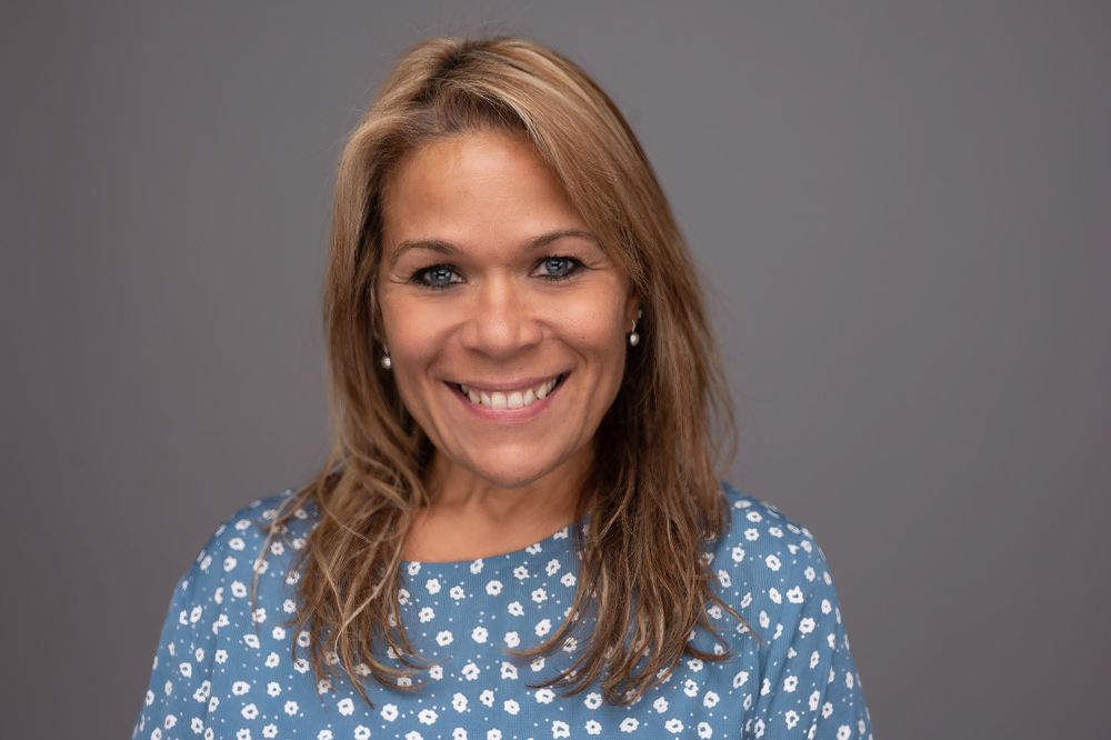 Professional headshot of woman in blue polka dot dress against gray background.