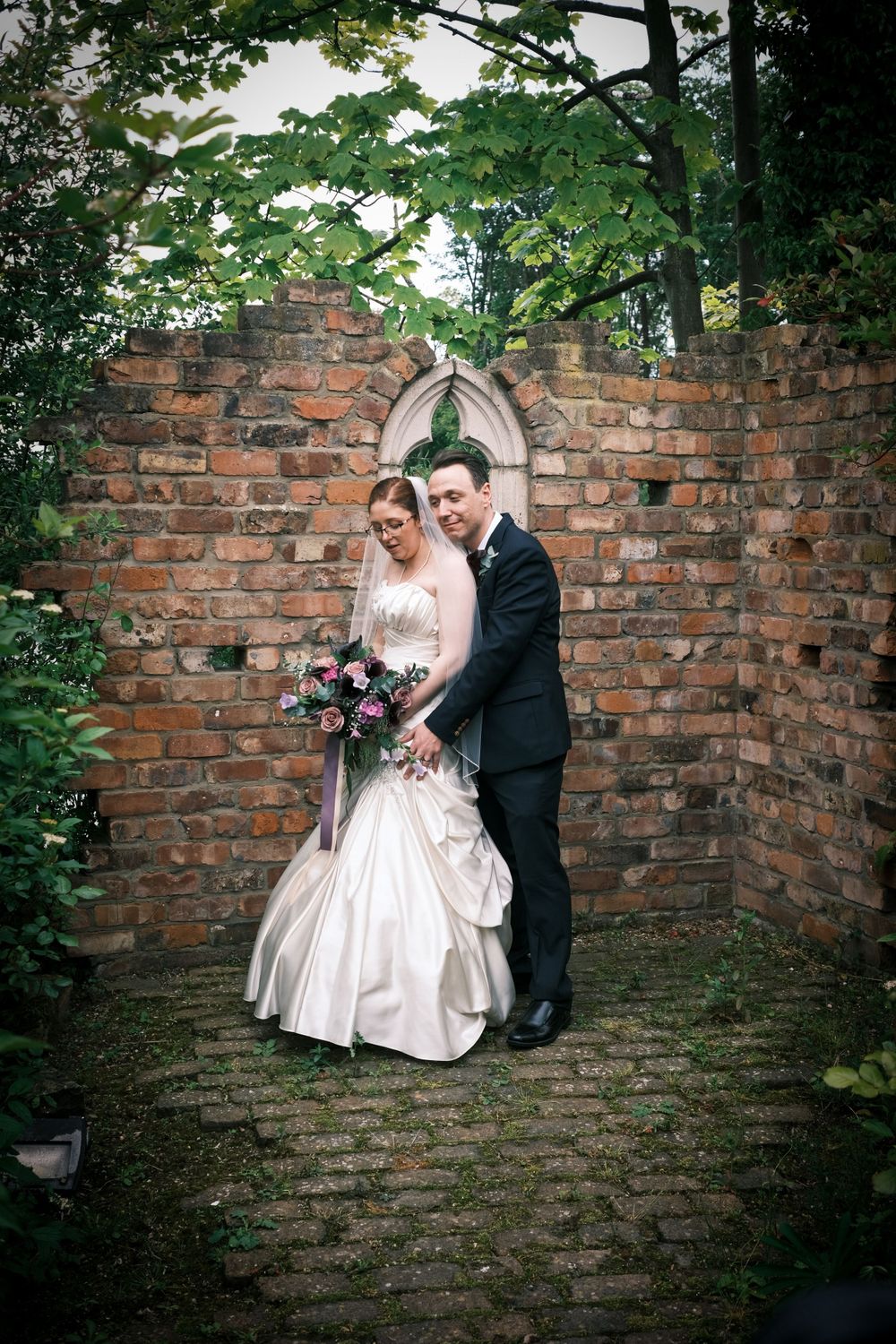 Romantic wedding portrait by gothic brick archway in garden setting.