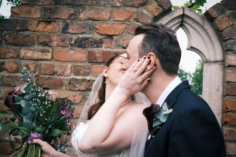 Tender moment captured between newlyweds against historic brick wall backdrop.