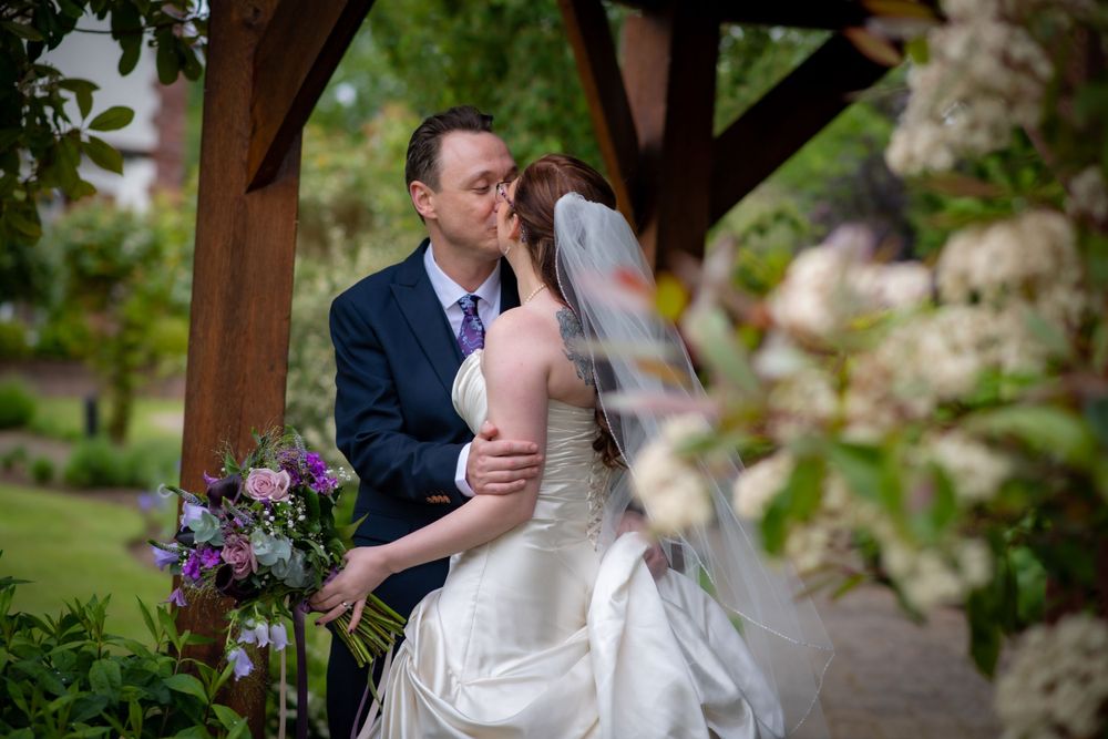 Romantic moment captured under wooden pergola in blooming garden setting.