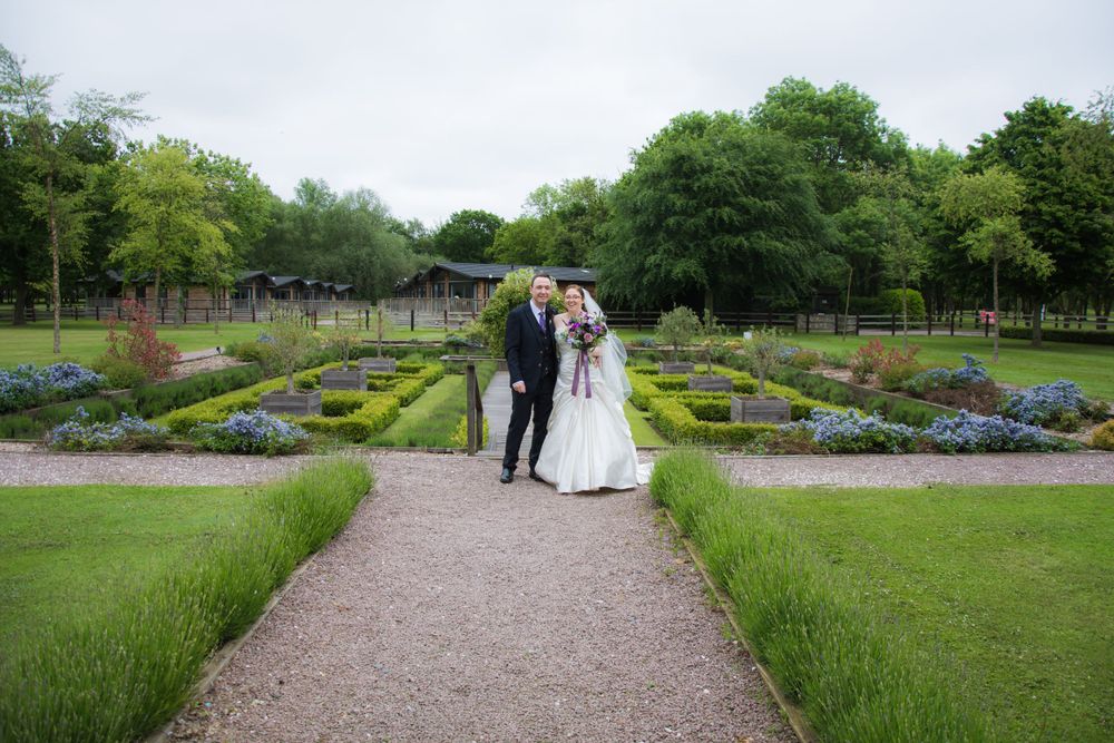 A couple walks along a gravel path in a beautiful formal garden with symmetrical flowerbeds.