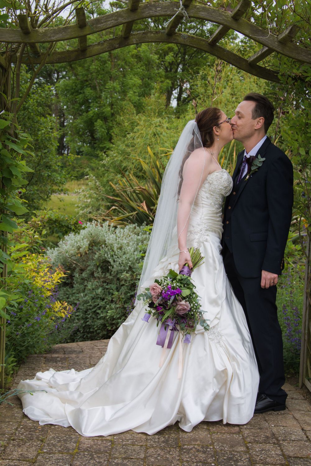 A romantic wedding scene under a garden arch with purple bouquet details.