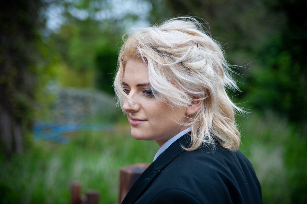 Portrait against a green garden background showing blonde hair styled in a casual updo.