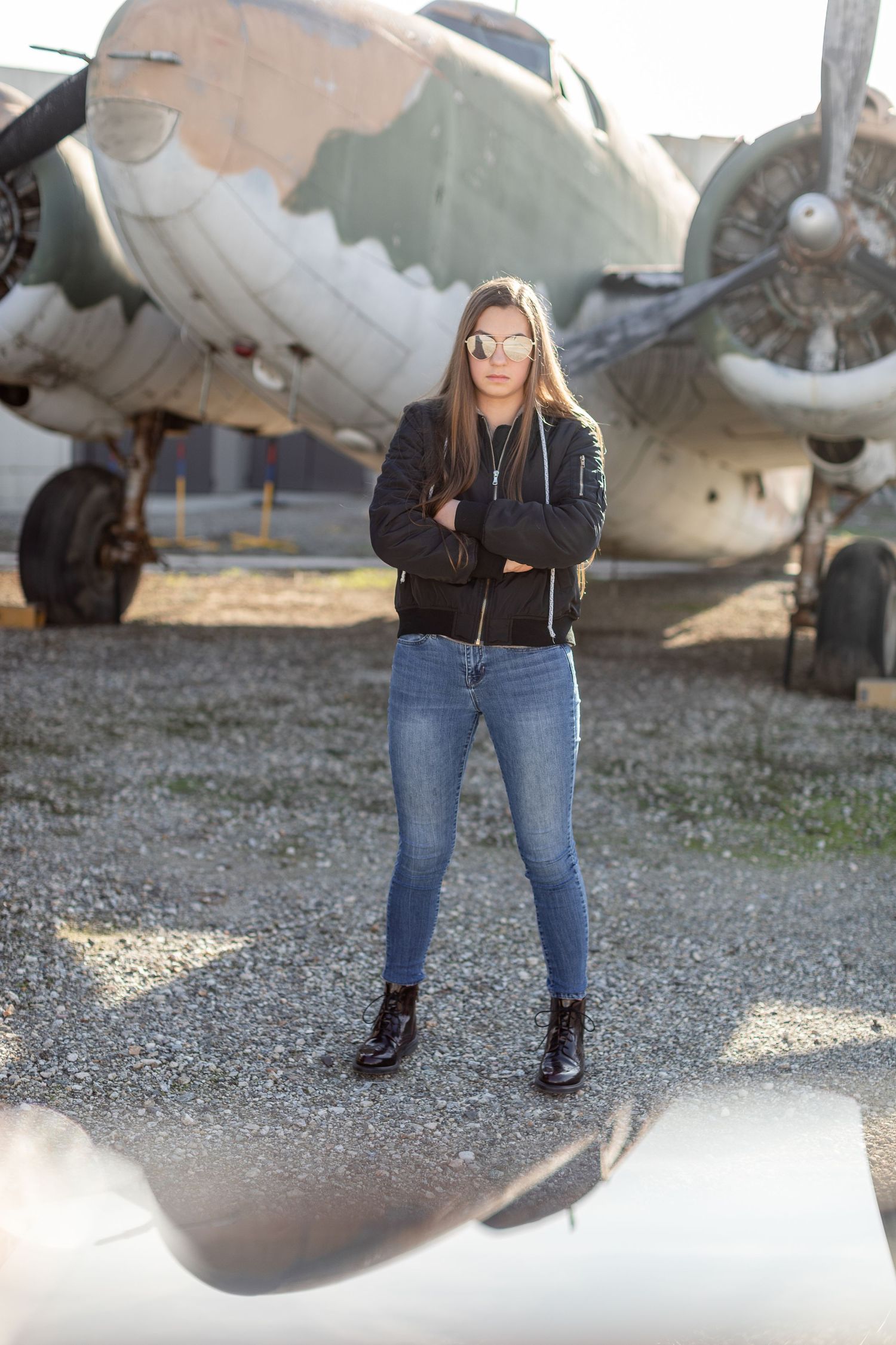 Teen girl standing with arms folded in a bomber jacket and Dr. Marten shoes wearing aviator sunglasses