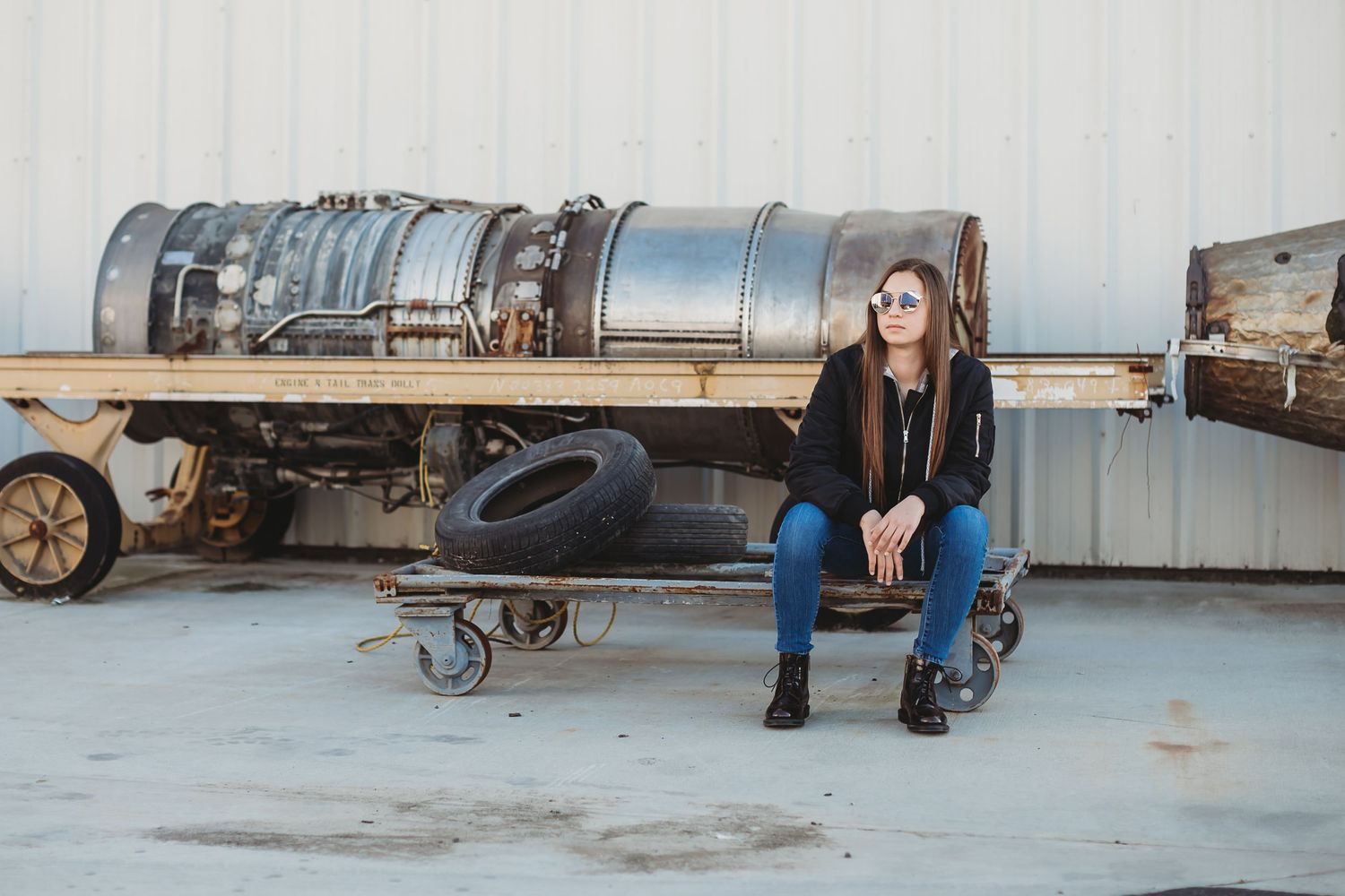 Girl sitting near airplane parts and old tires wearing aviator sunglasses
