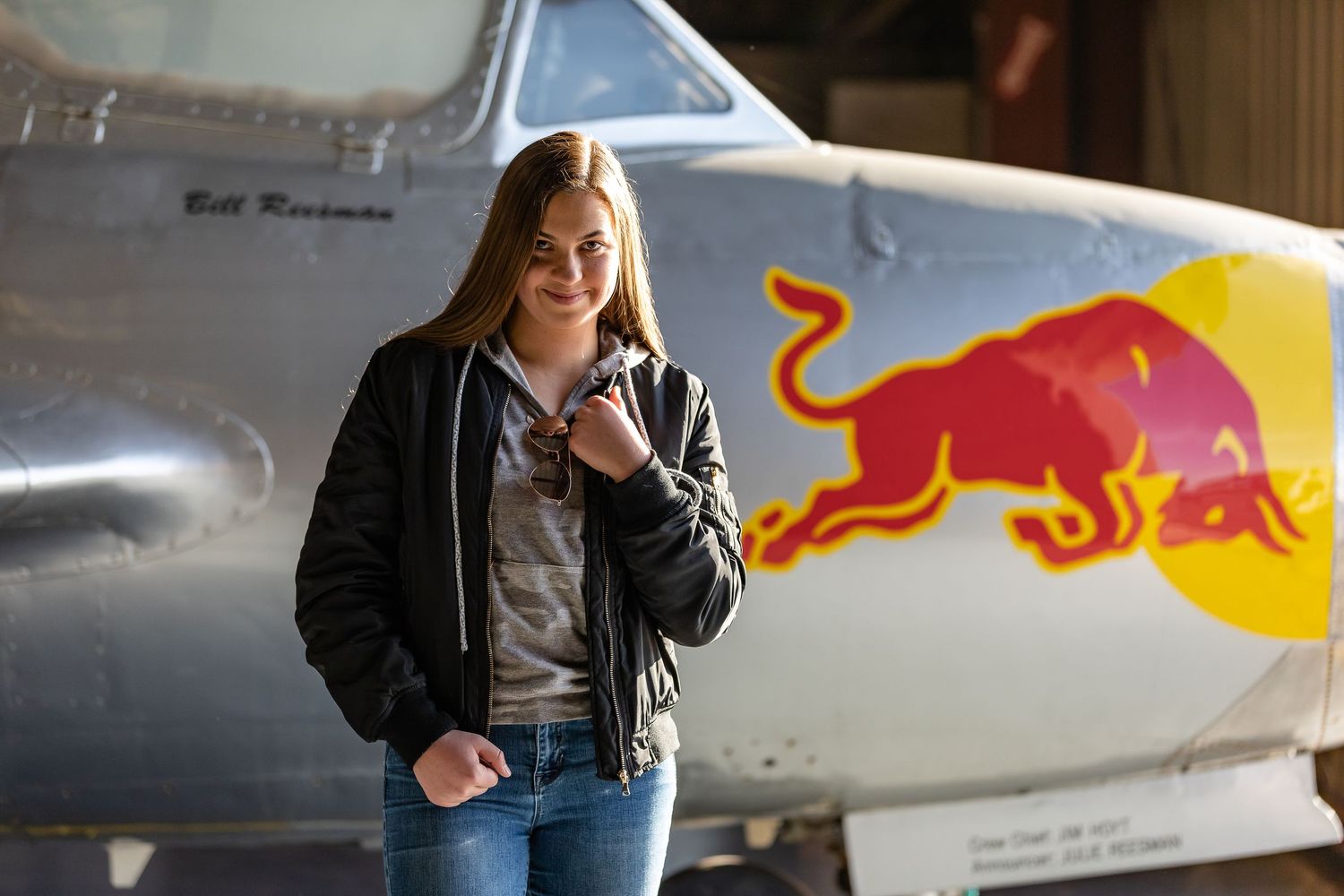 Girl in bomber jacket standing in front of Red Bull airplane