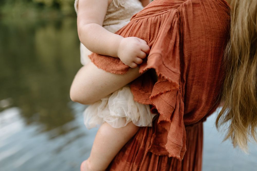 close up detail image of mom holding baby girl. Baby is holding onto ruffled sleeve of moms dress