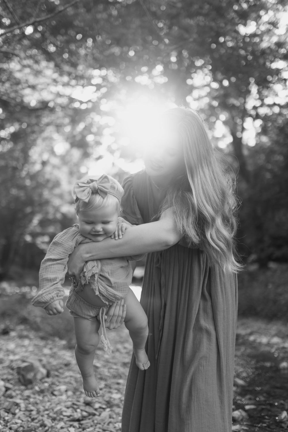 Momma and baby girl play in a small pebble bottomed creek as the dreamy sunlight filters through the surrounding trees