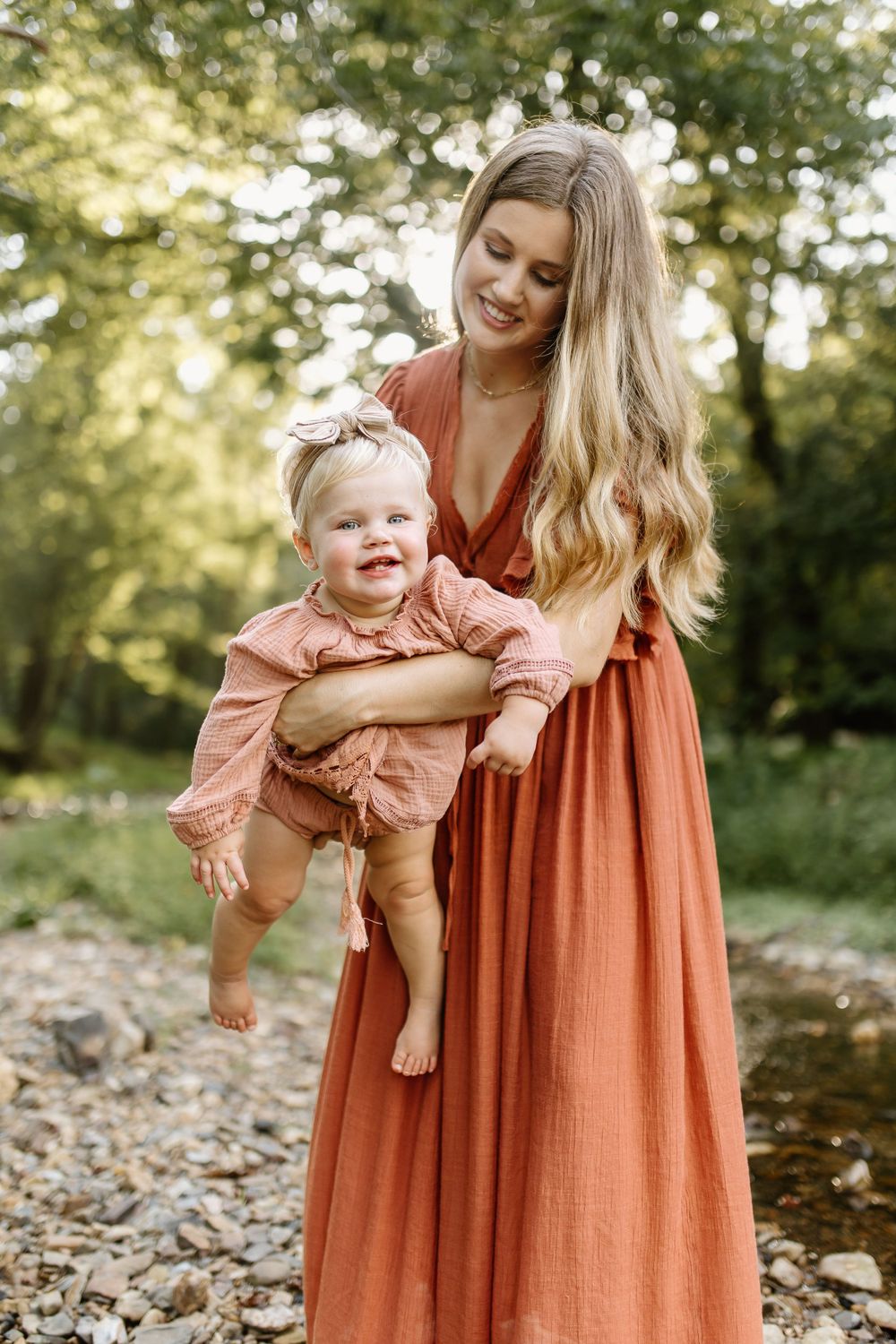 Momma and baby girl play in a small pebble bottomed creek as the dreamy sunlight filters through the surrounding trees