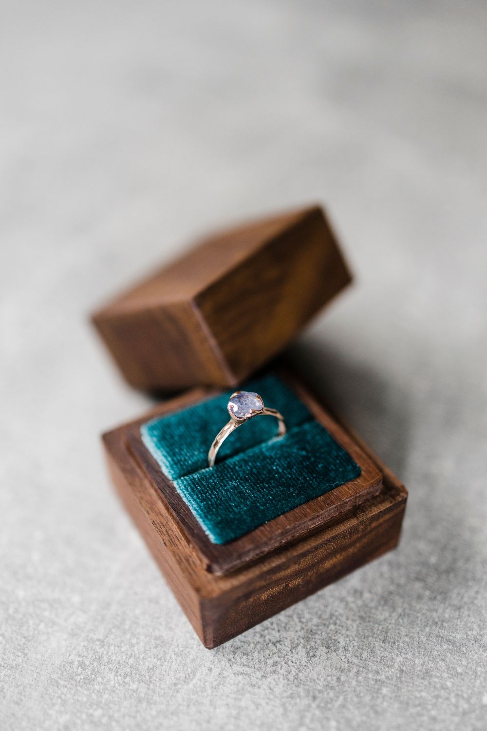 Diamond engagement ring in small wooden box with teal velvet cushion.
