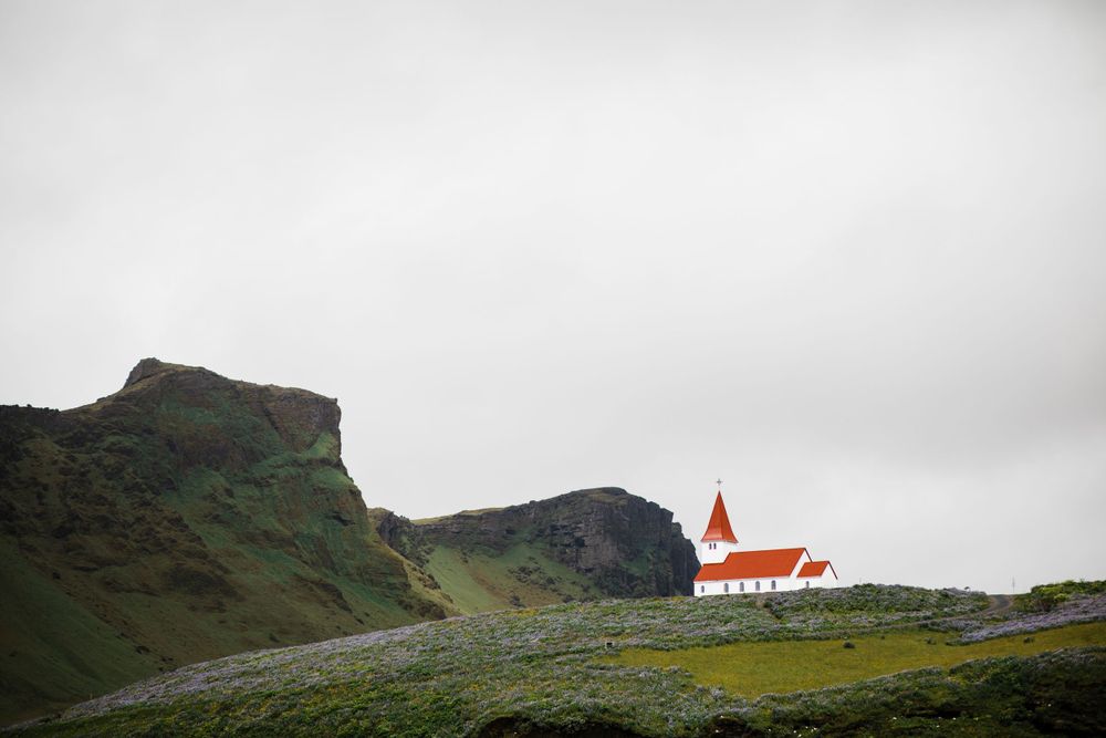 Row of identical A-frame cottages reflected in still water beneath dramatic mountain landscape.