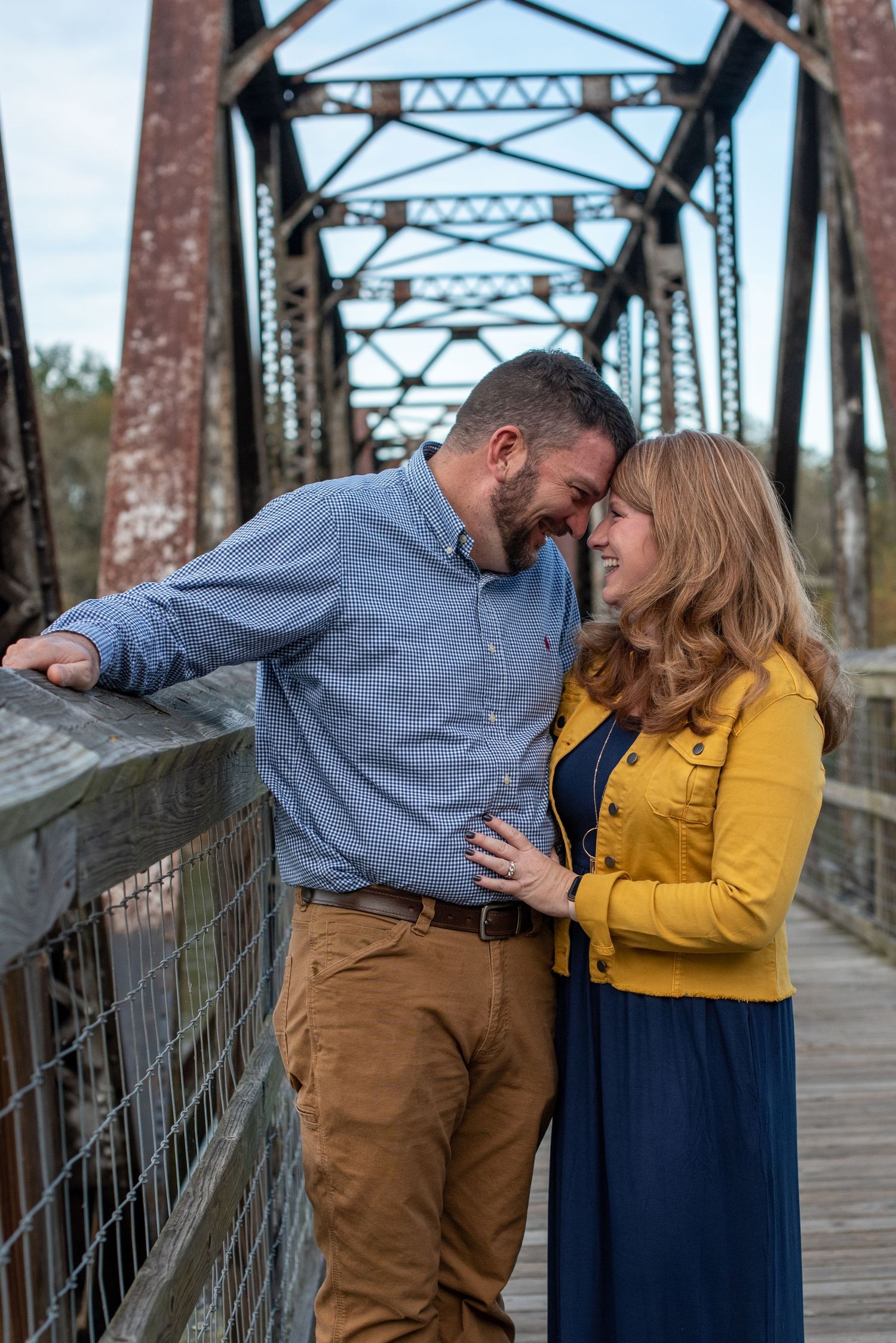 Couple sharing romantic moments on a rustic metal bridge wearing yellow and blue outfits.