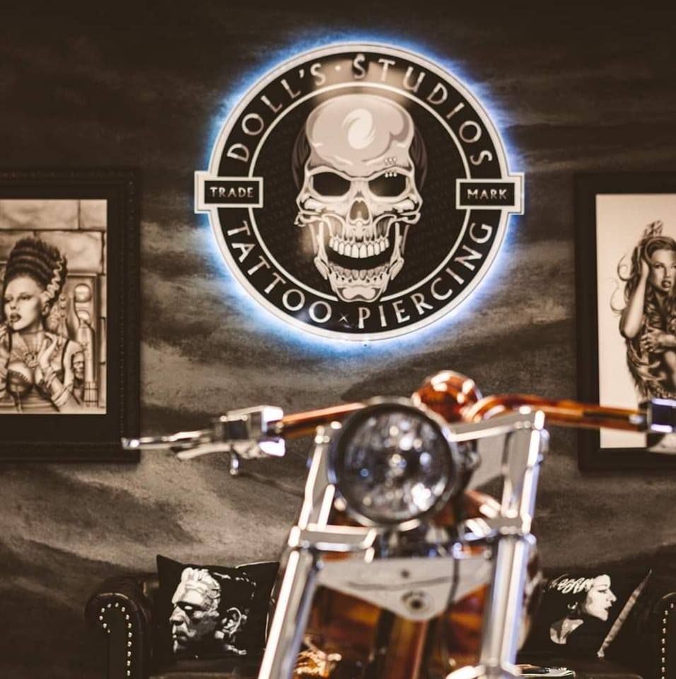 Dolis Studios Tattoo and Piercing neon skull logo sign above a vintage motorcycle.
