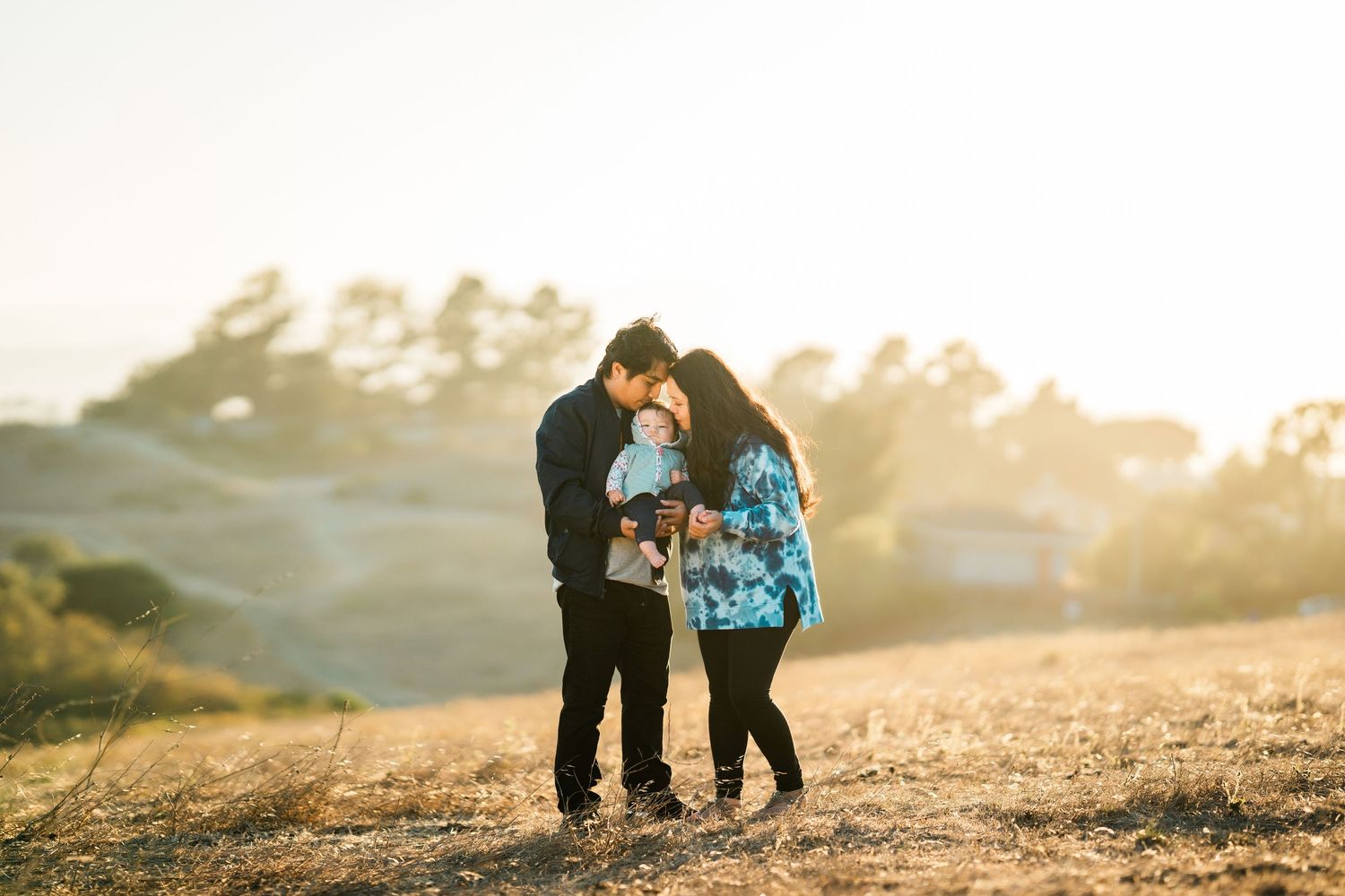 A couple shares an intimate moment with their dog at sunset on a hilltop during golden hour.