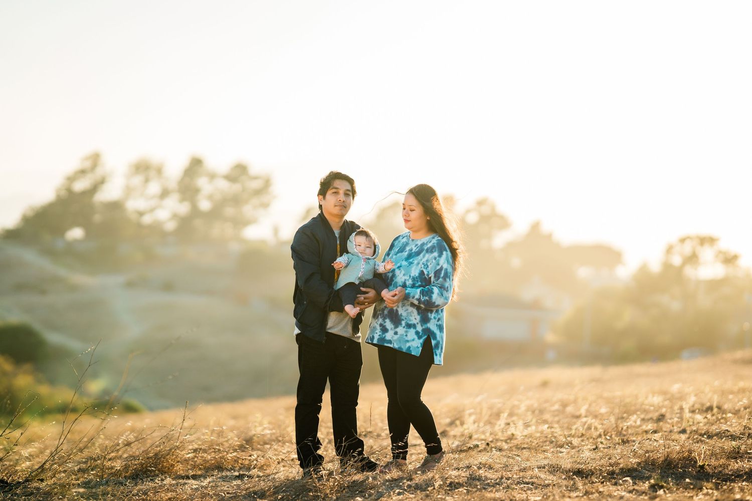 Couple walking together with their small dog on a sunlit hilltop during golden hour.