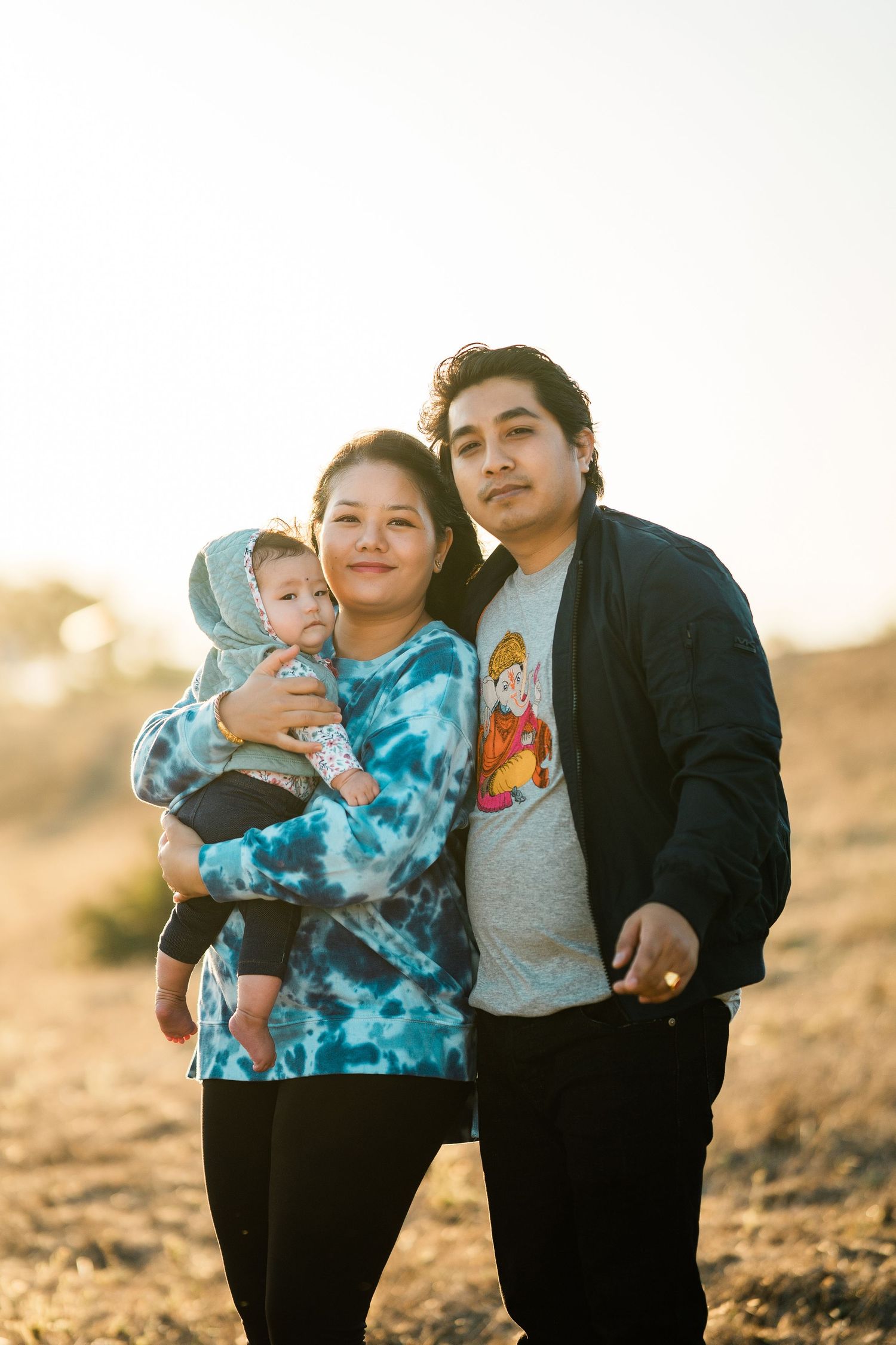 Family of three poses together outdoors during golden hour in the desert with warm sunset lighting.