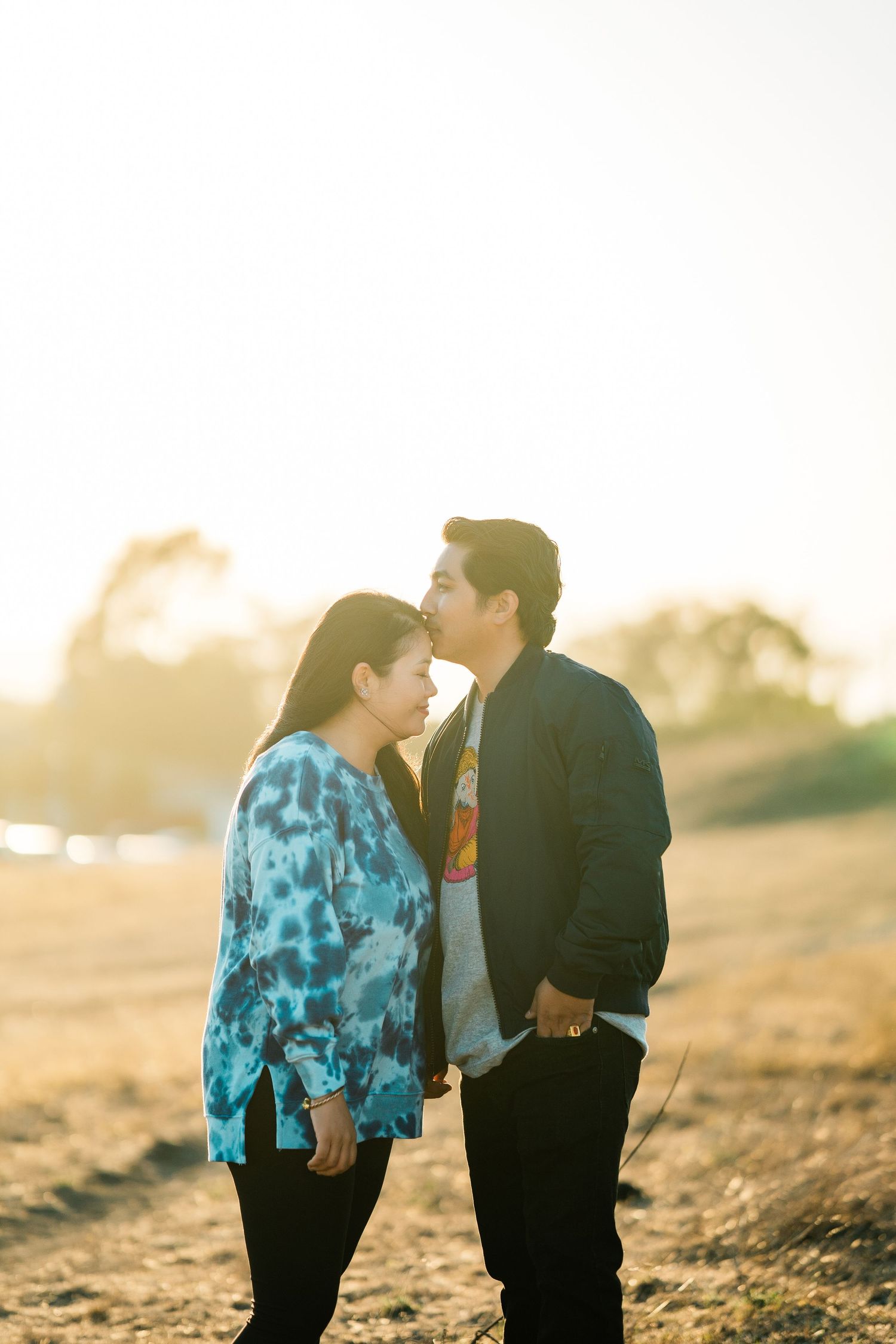 A couple shares an intimate moment at sunset in a field with warm golden light glowing behind them.