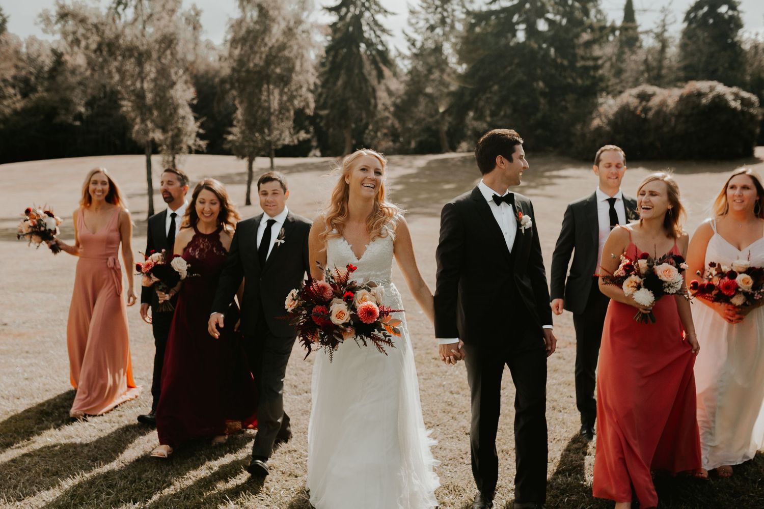 Wedding party poses together outdoors with bridesmaids in coral and red dresses.