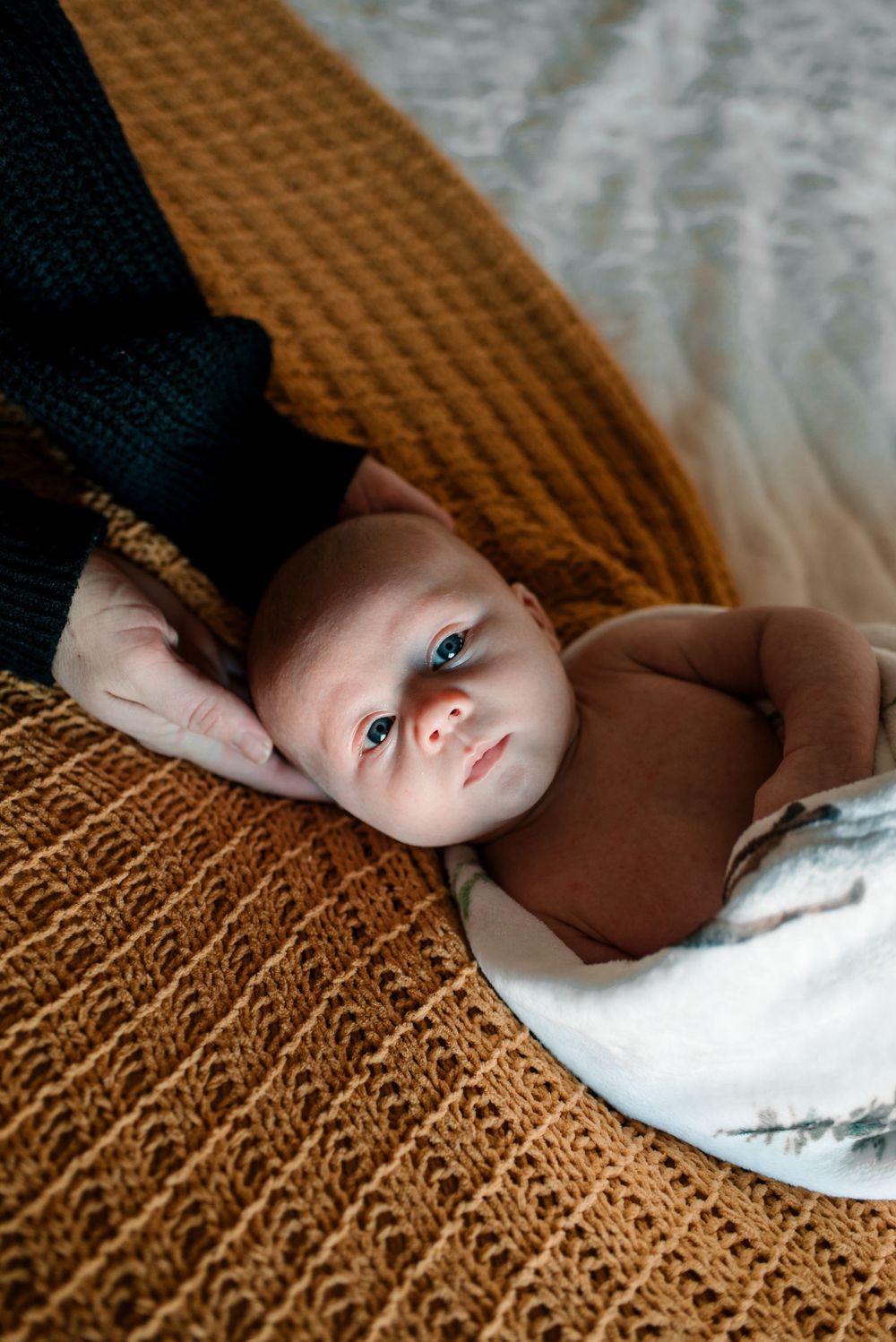 Baby in brown clothing resting on a textured caramel-colored blanket.
