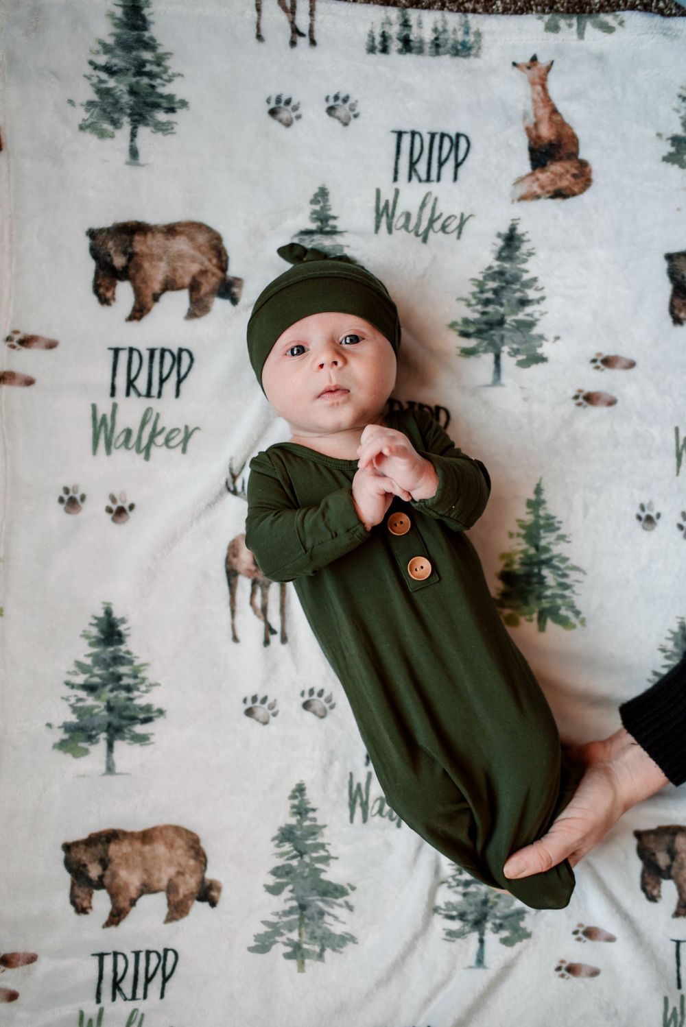 Infant in green sleepwear on forest-themed blanket with wildlife illustrations.