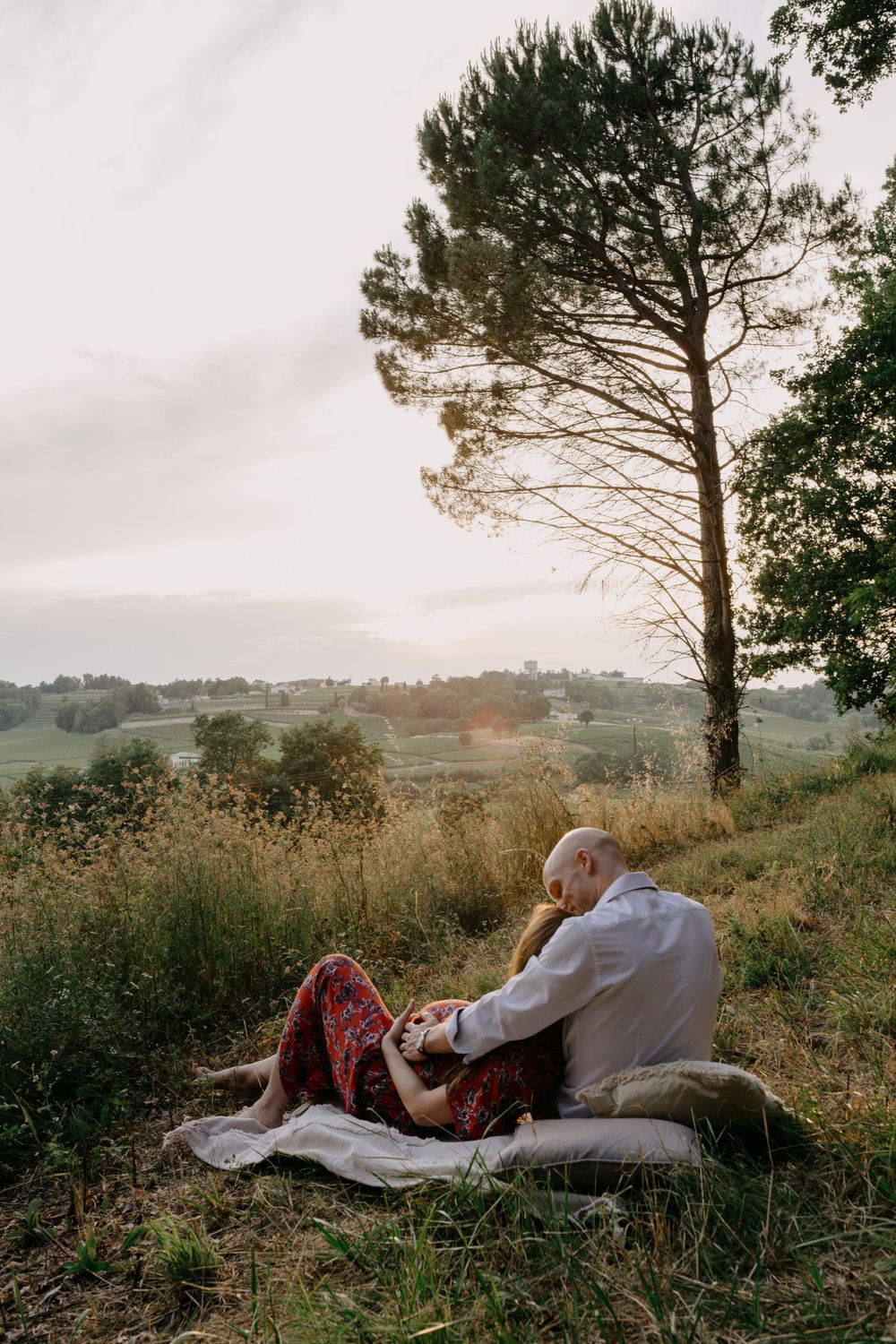 Couple sharing peaceful moment on blanket against scenic countryside sunset.