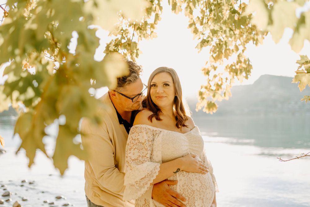 Beautiful lakeside maternity session under golden autumn leaves with soft natural lighting.