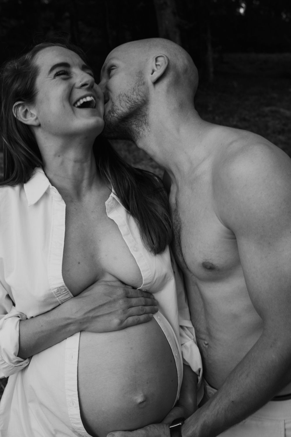 Black and white intimate portrait capturing joyful moment between expectant couple.