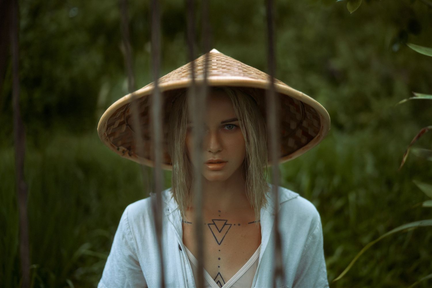 Atmospheric portrait with traditional Asian conical hat in forest setting.