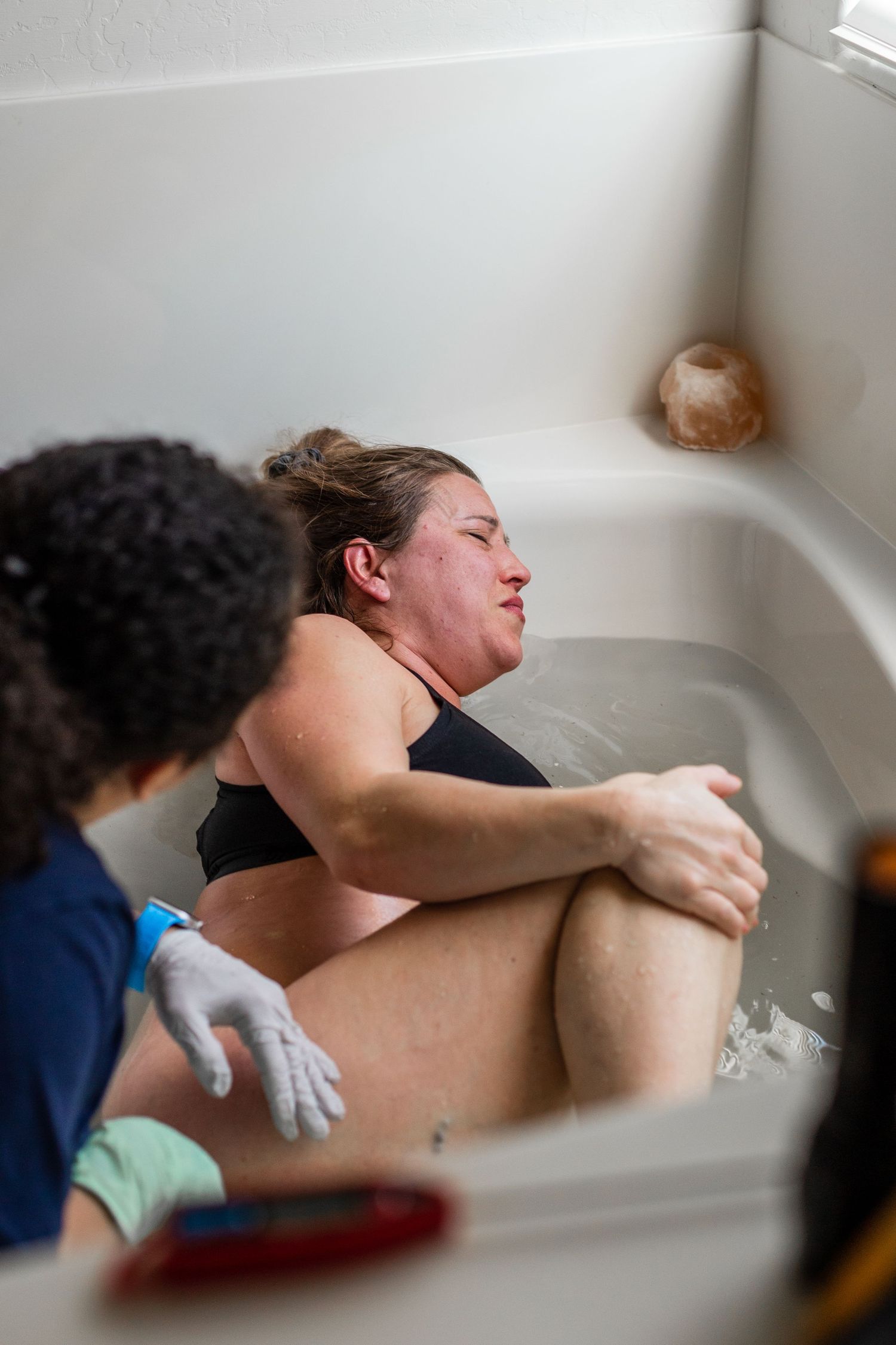 Person in labor receiving support in a bathtub during childbirth.