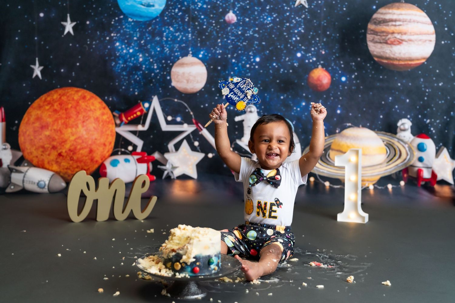 Happy baby celebrating first birthday with cake smash against space backdrop.