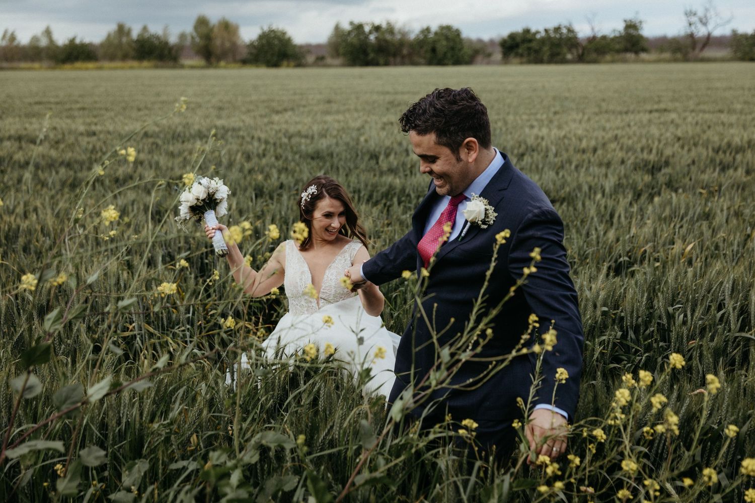 A couple walks through a flowering field during their rustic outdoor wedding.