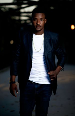 Professional portrait of a man in a navy blazer and white t-shirt against a dark background.
