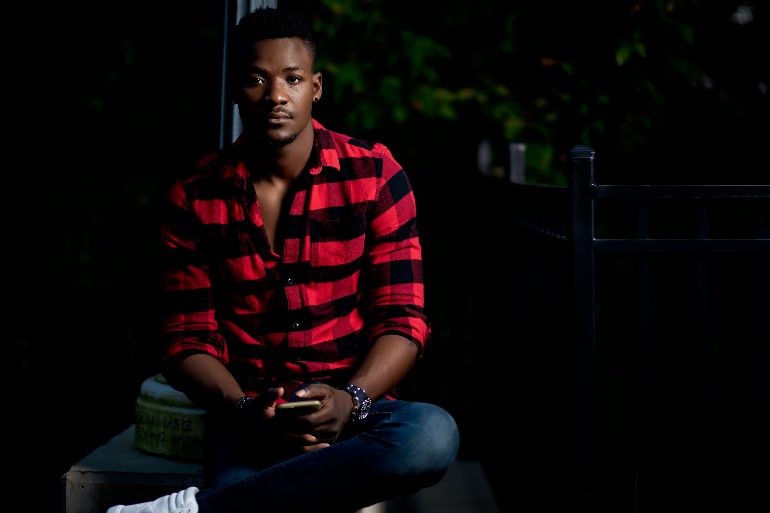 Portrait of a person wearing a red and black plaid shirt in a moody, dimly lit setting.
