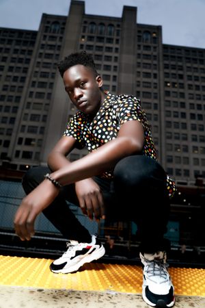 Fashion portrait of person in polka dot shirt squatting against urban backdrop.