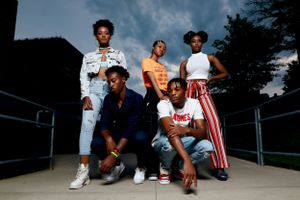 Group of five people in casual outfits pose together outdoors at dusk.