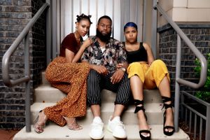 Three people in trendy outfits pose together on concrete steps.