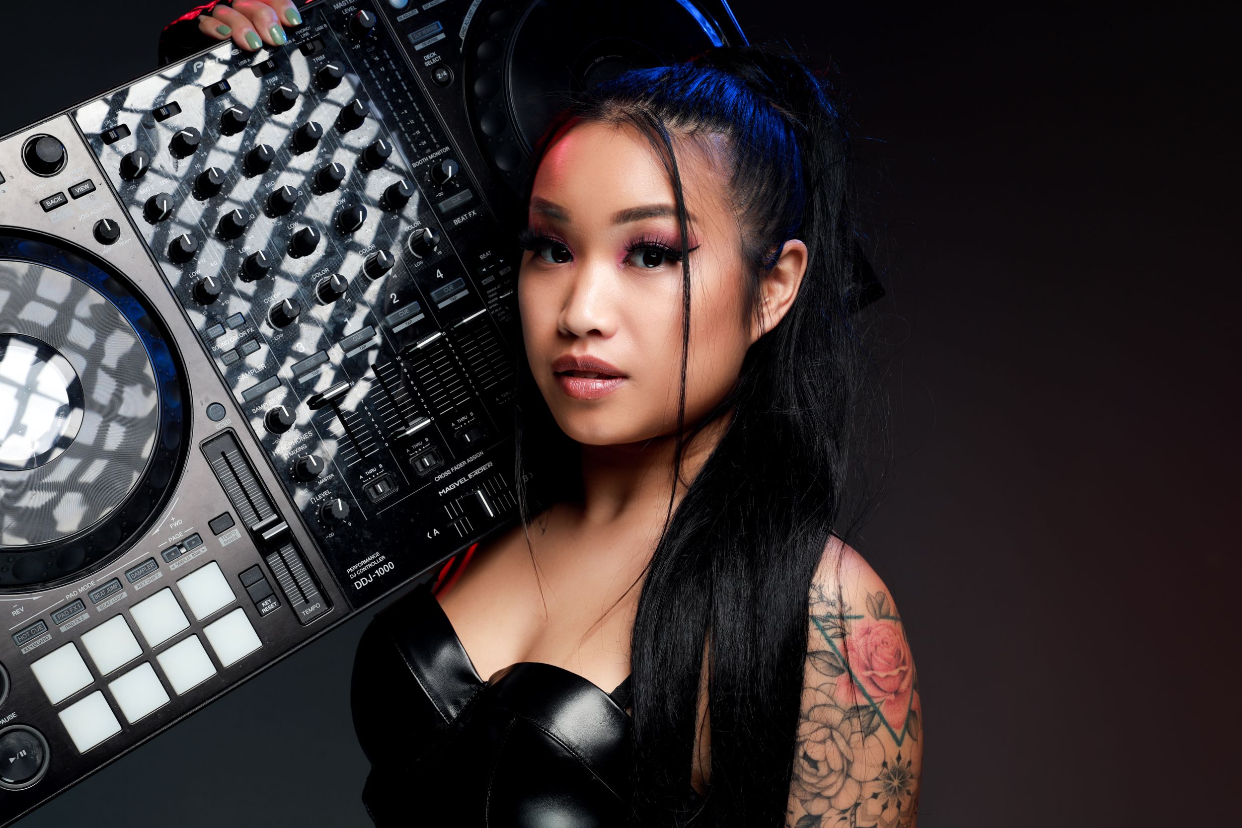 Female DJ posing with professional mixing equipment and colorful hair.
