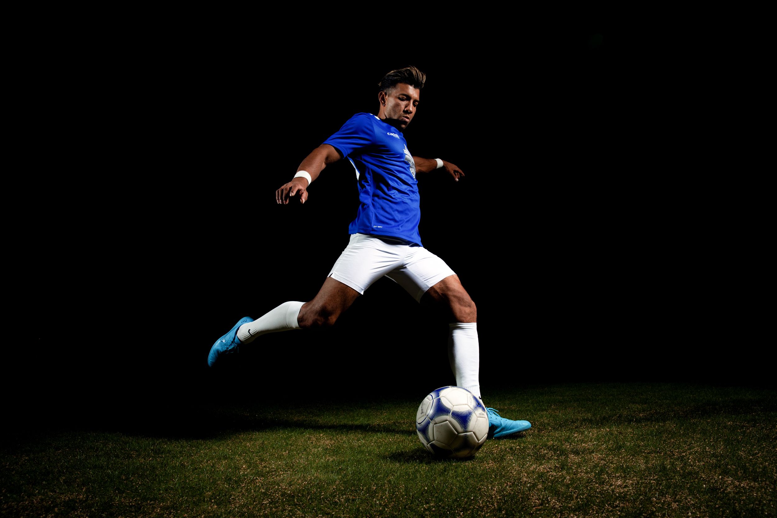 Action shot of soccer player kicking ball in blue jersey at night.