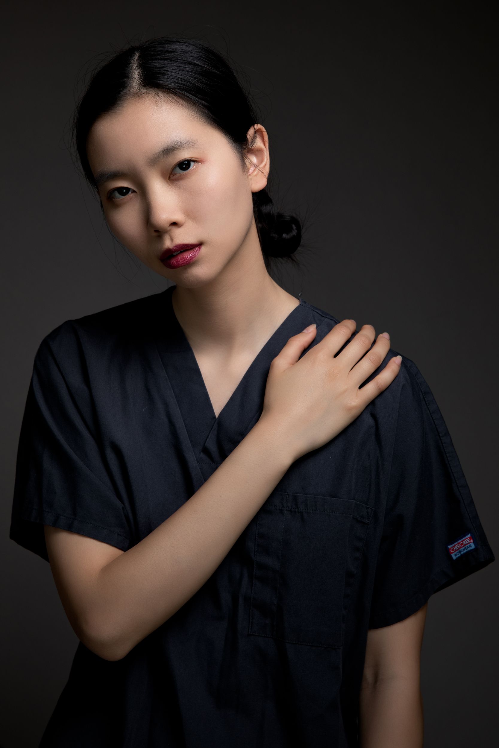 Professional headshot in navy medical scrubs against dark background.