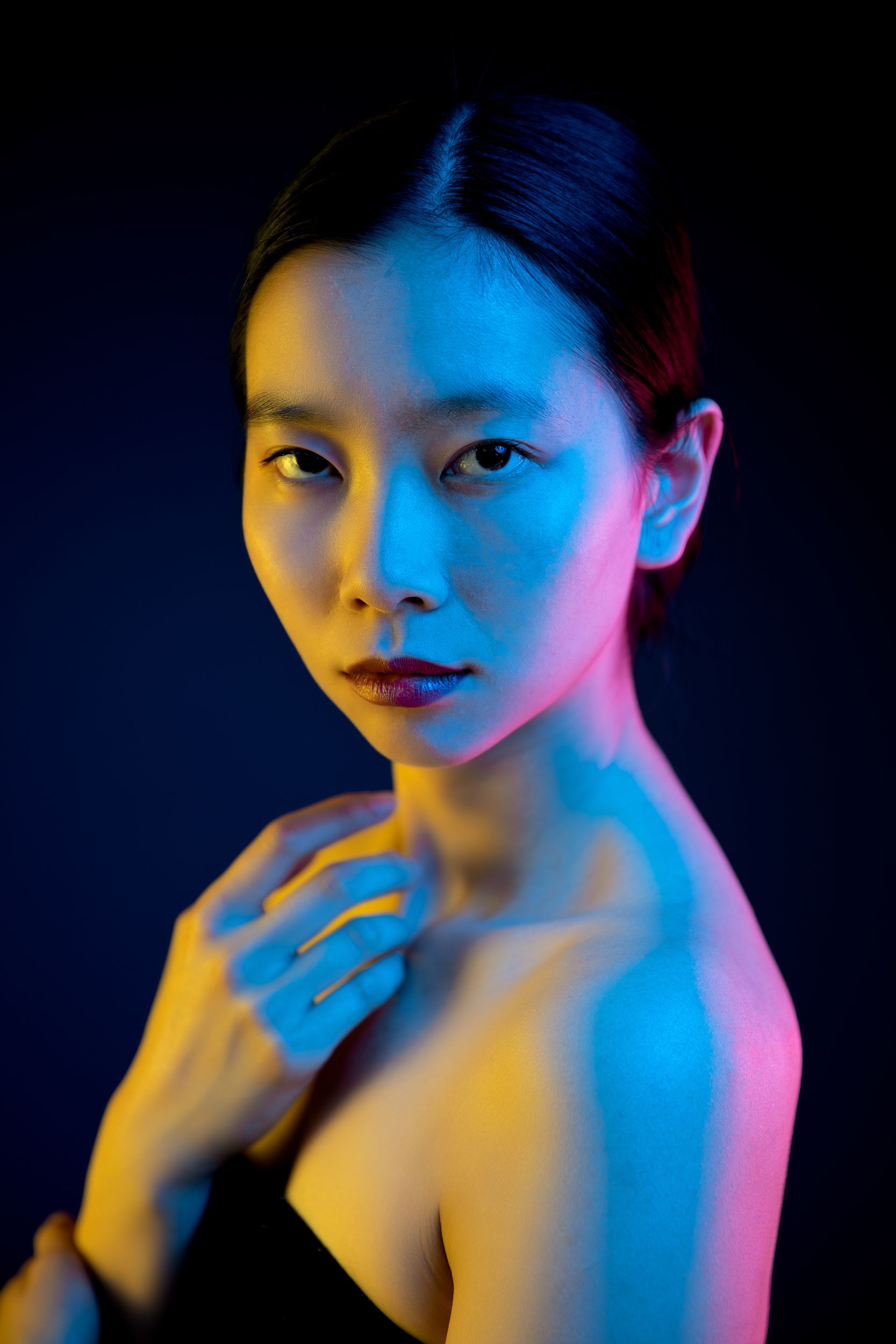 Studio portrait featuring dramatic colored lighting with blue and orange gels against black background.