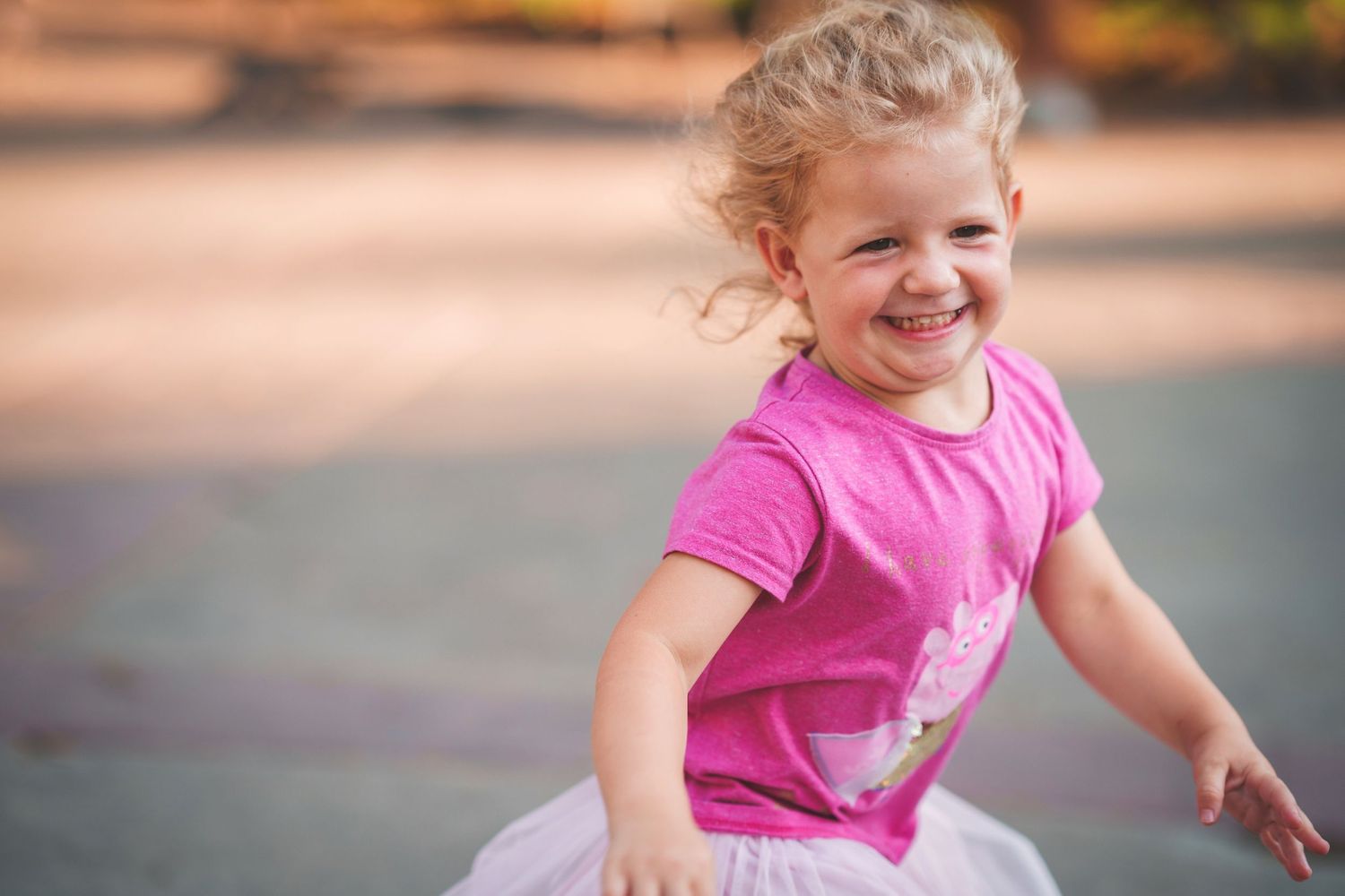 Child in pink shirt and tulle skirt dancing and playing outdoors.