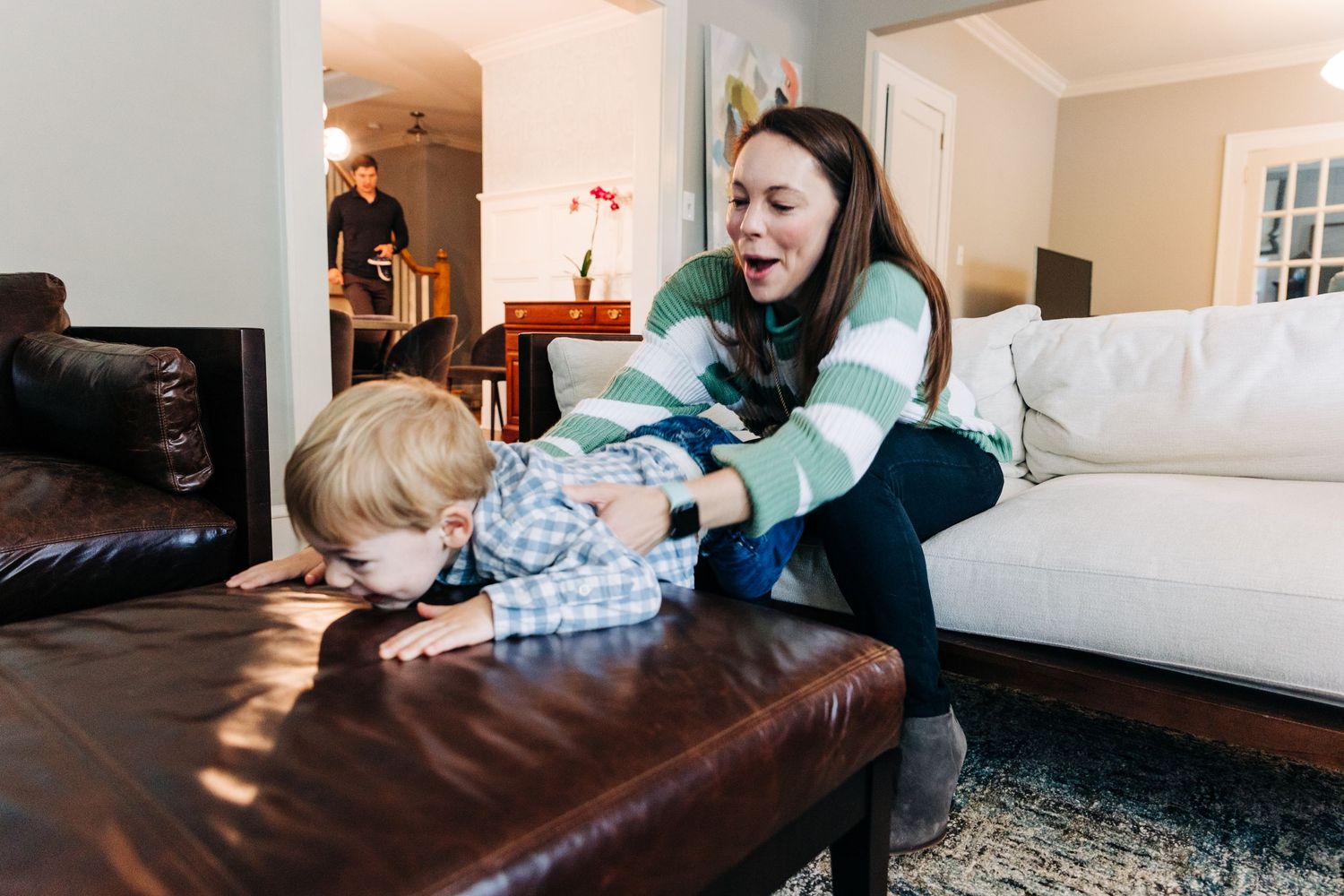 Mom laughing and trying to pick up her son who is trying to crawl away smiling