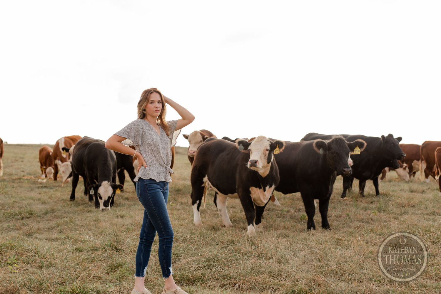 Casual country photoshoot with herd of cattle grazing in background.