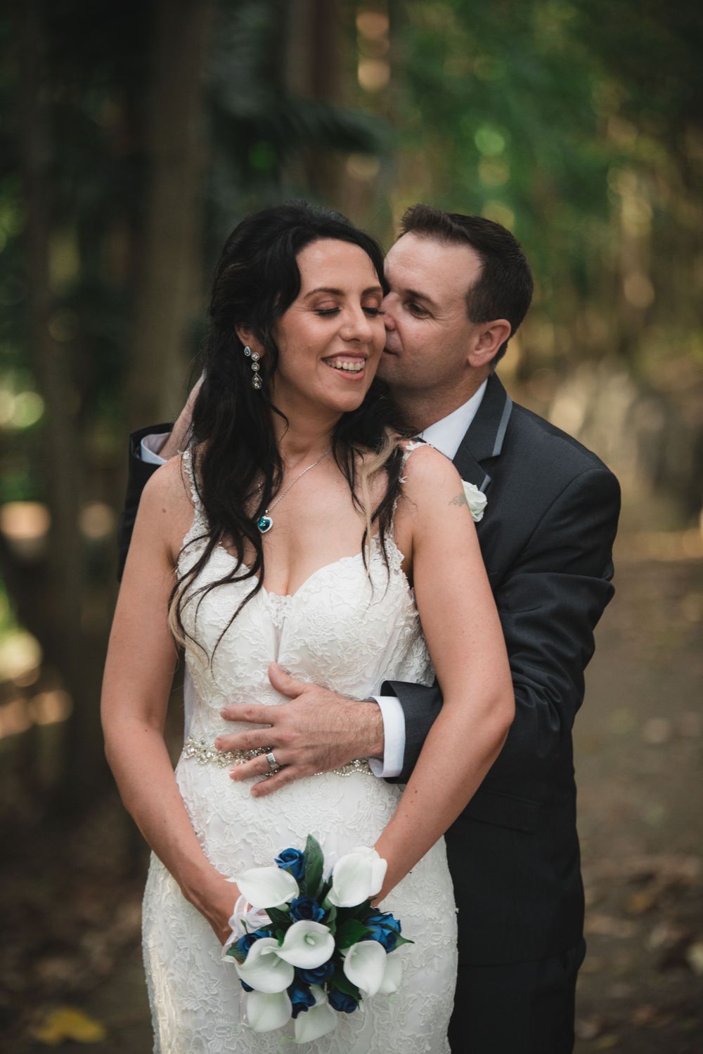 Intimate wedding portrait with white calla lily bouquet in wooded setting.