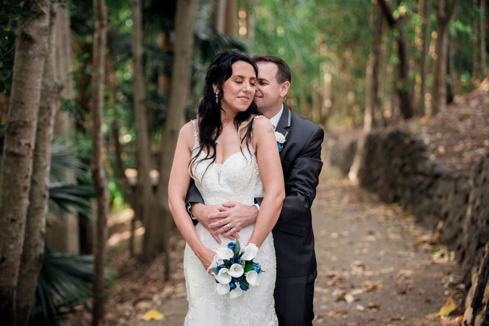Romantic forest wedding photo with couple embracing while holding a white and blue bouquet.